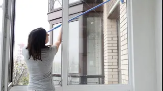 Woman cleaning a large window with a squeegee, showcasing her effort to maintain a tidy home environment. Natural light filters in, enhancing the setting.